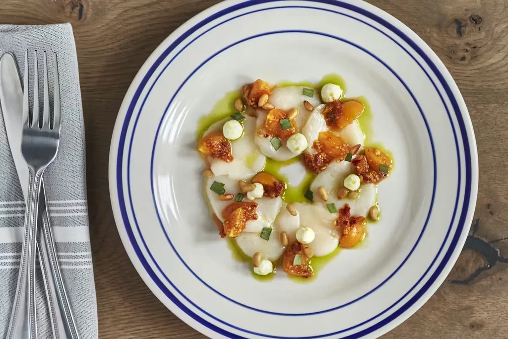Overhead view: Plated white slices, green oil, garnishes on rustic wood.