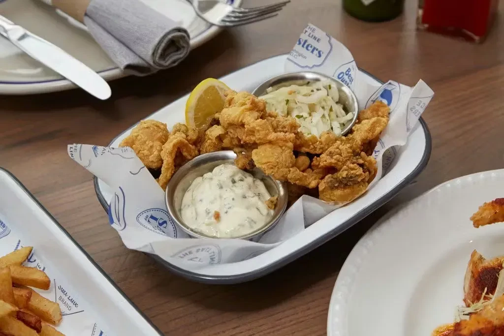 Golden fried seafood, tartar sauce, coleslaw, and fries on a wooden table.