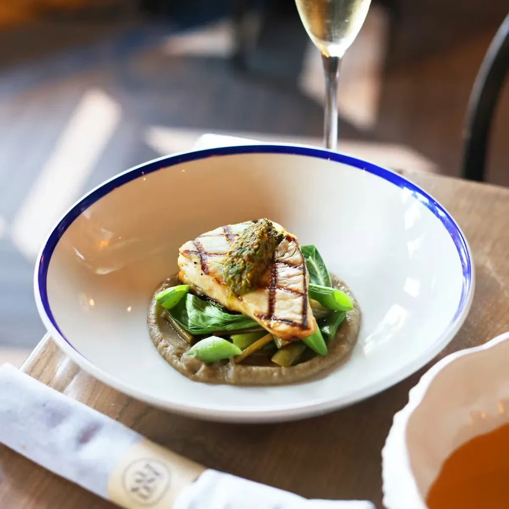 Grilled fish with pesto on greens in a blue-striped bowl.