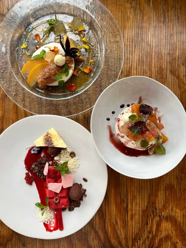 Overhead view of three artfully plated gourmet desserts on a rustic wooden table.