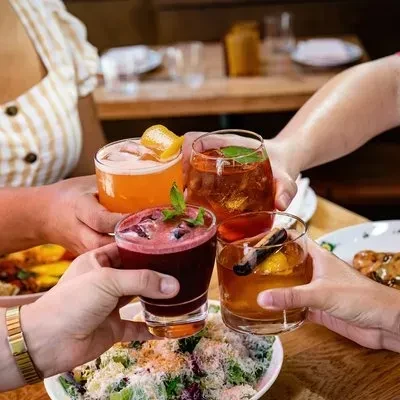 Four hands toasting with diverse, colorful cocktails and food.