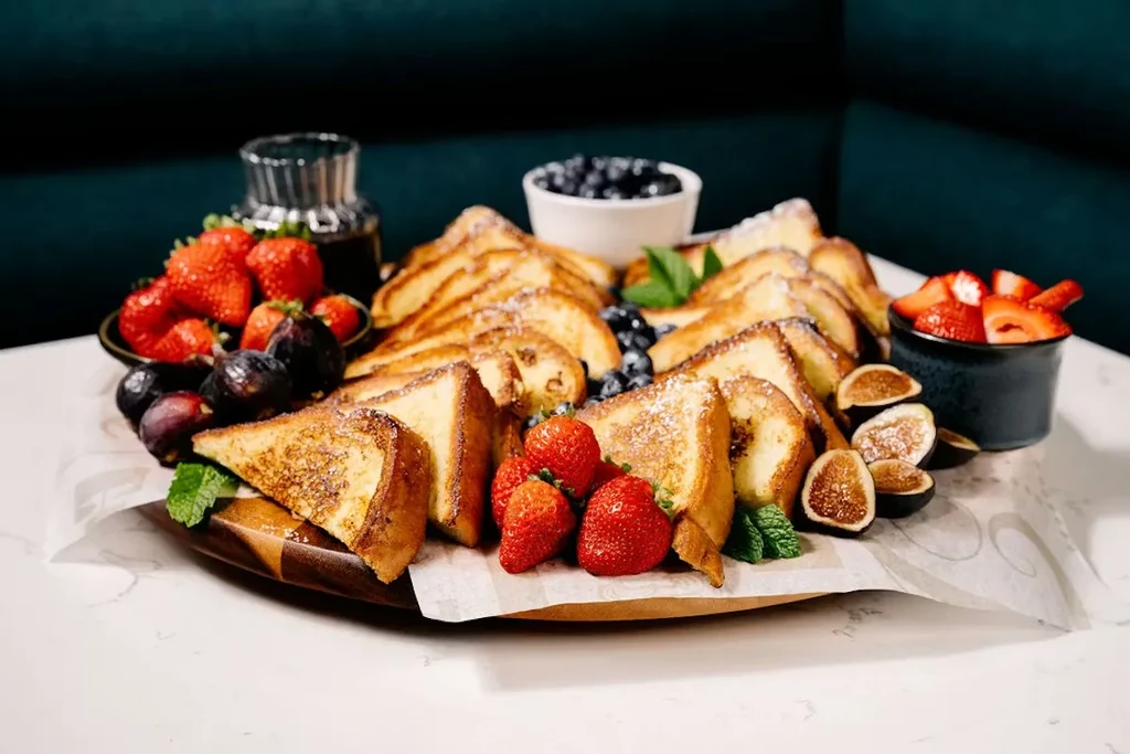 Golden French toast with strawberries, figs, blueberries, and syrup.