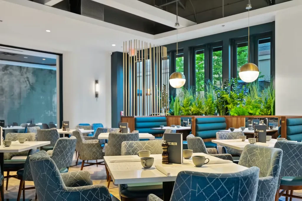 Contemporary restaurant with white tables, patterned chairs, teal booths, and plants.