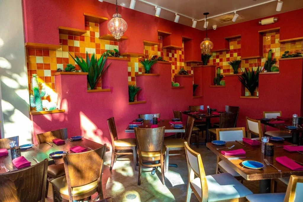 Vibrant restaurant interior with red walls, plants, and set wooden tables.