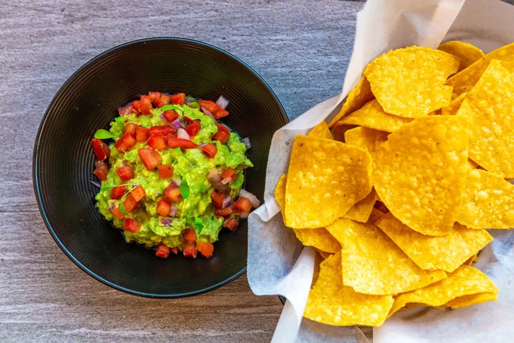 Overhead: Chunky guacamole topped with tomatoes, beside crisp tortilla chips.