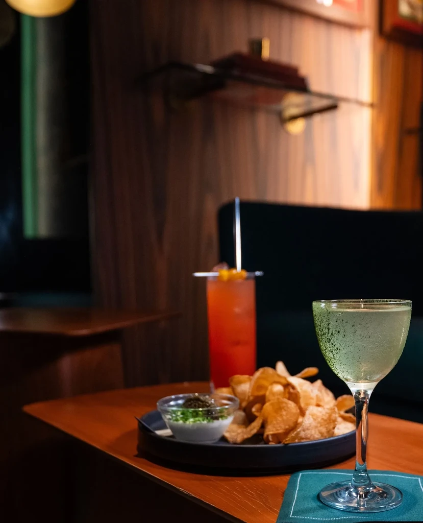 Two cocktails, chips, and dip in a sophisticated bar setting.