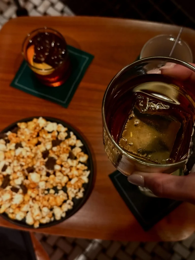 Hand holds drink, snacks, and cocktail on a wooden table.