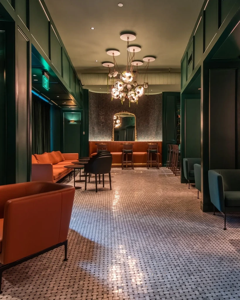 Elegant, dim-lit lounge with green walls, chandelier, and orange seating.