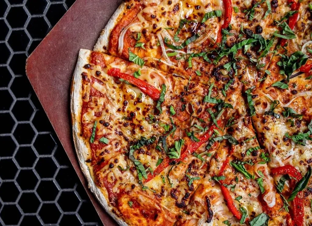 Freshly baked pizza with cheese, bell peppers, onions, and green herbs.