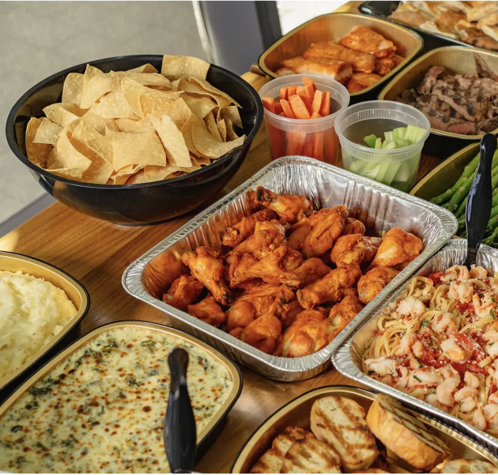 Bountiful buffet with chicken wings, pasta, salmon, and assorted side dishes.