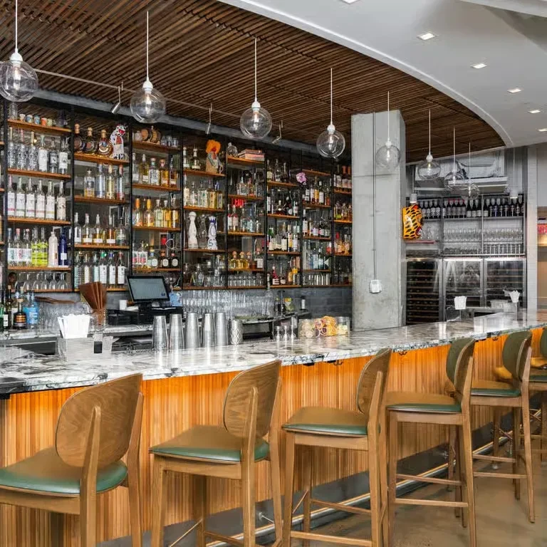 Well-lit modern bar with marble counter, tiered liquor display, and green stools.