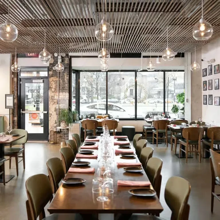 Modern restaurant interior with a long communal table and city view.