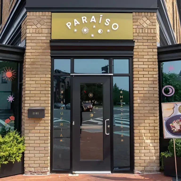 Exterior of Paraiso Taqueria Mezcaleria with brick facade and olive-green sign.