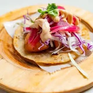 Fried fish taco with slaw, pickled onions, and sauce on wood.