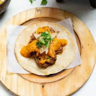 Shredded meat taco with creamy orange sauce, diced onion, and cilantro.