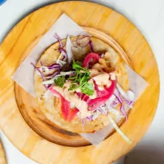 Soft taco with cabbage, pink pickled onions, sauce, cilantro, on wooden plate.