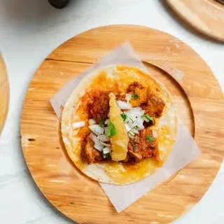 Taco with meat, onions, cilantro, and pineapple on a wooden board.