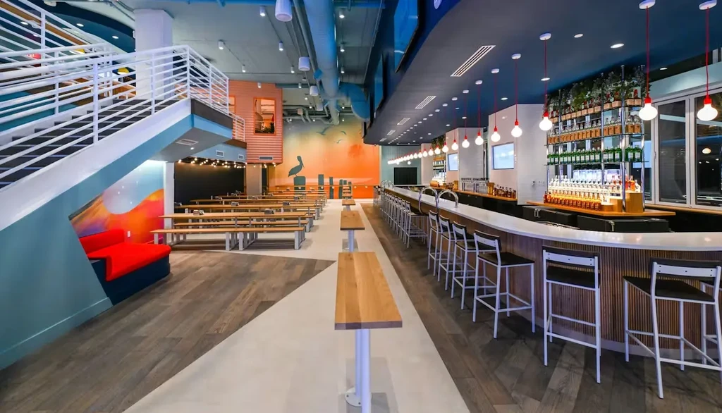 Empty, modern restaurant interior featuring a bar, communal tables, and murals.