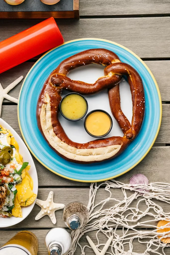 Soft pretzel, nachos, and beach decor on rustic wooden table.