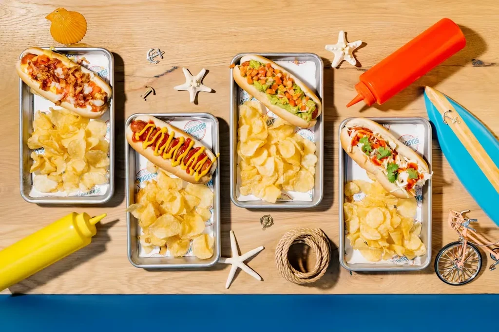 Hot dogs with varied toppings and chips on a boardwalk-themed table.