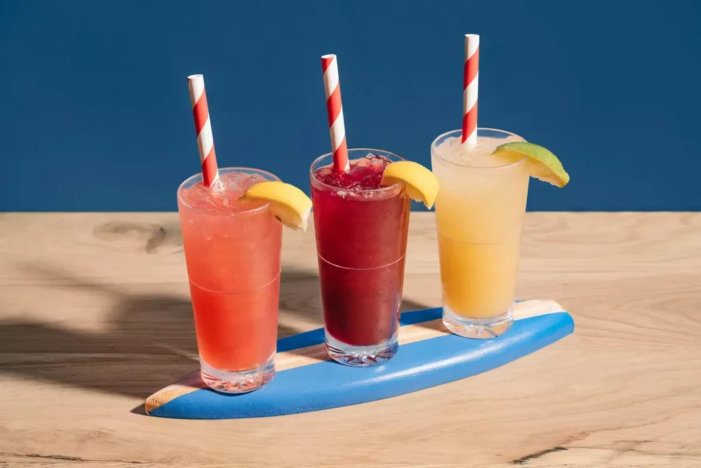 Three colorful iced drinks with citrus and straws on a blue tray.