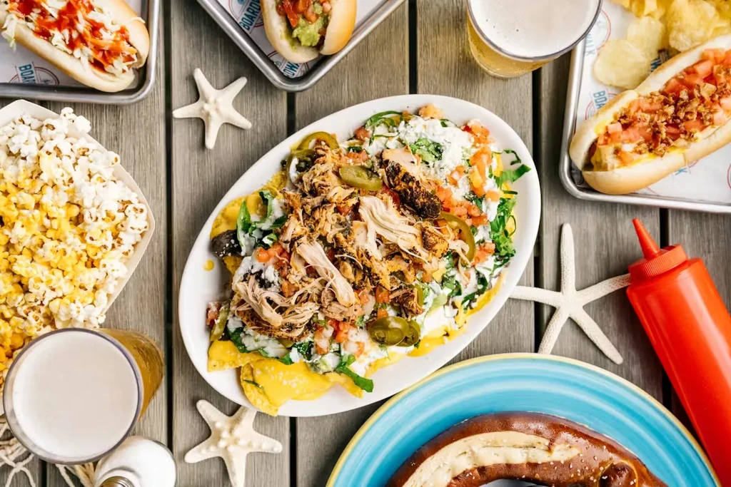 Overhead: Loaded nachos, hot dogs, pretzel, beer, popcorn, starfish on wood.