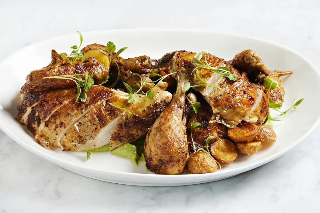 Plated roasted chicken, carved with crispy skin, potatoes, and green sauce.