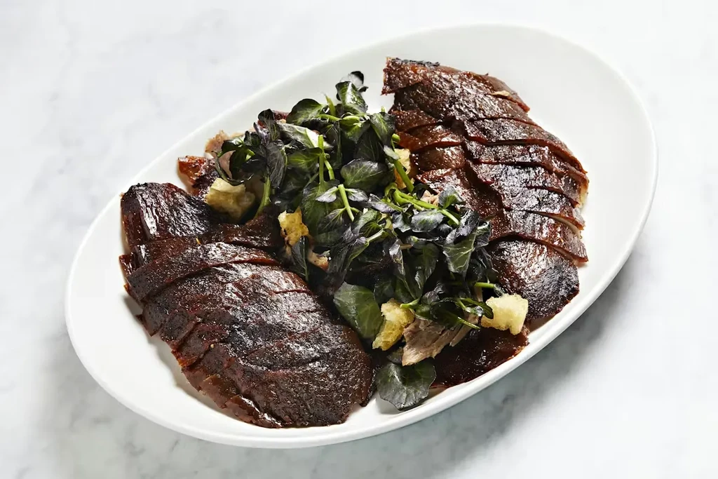 Sliced dark-glazed poultry, greens, and crispy garnish on an oval platter.