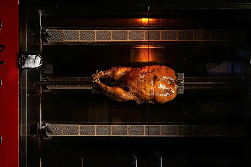 Roasted chicken rotating on a rotisserie inside an oven.