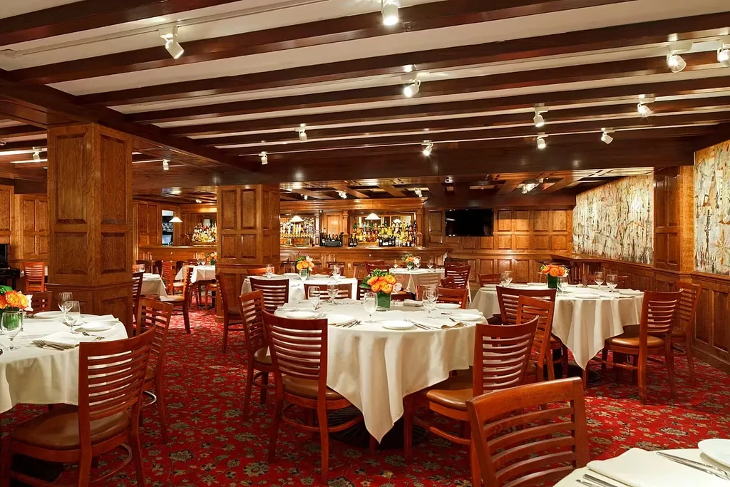 Empty restaurant dining area with set tables, wood paneling, and bar.