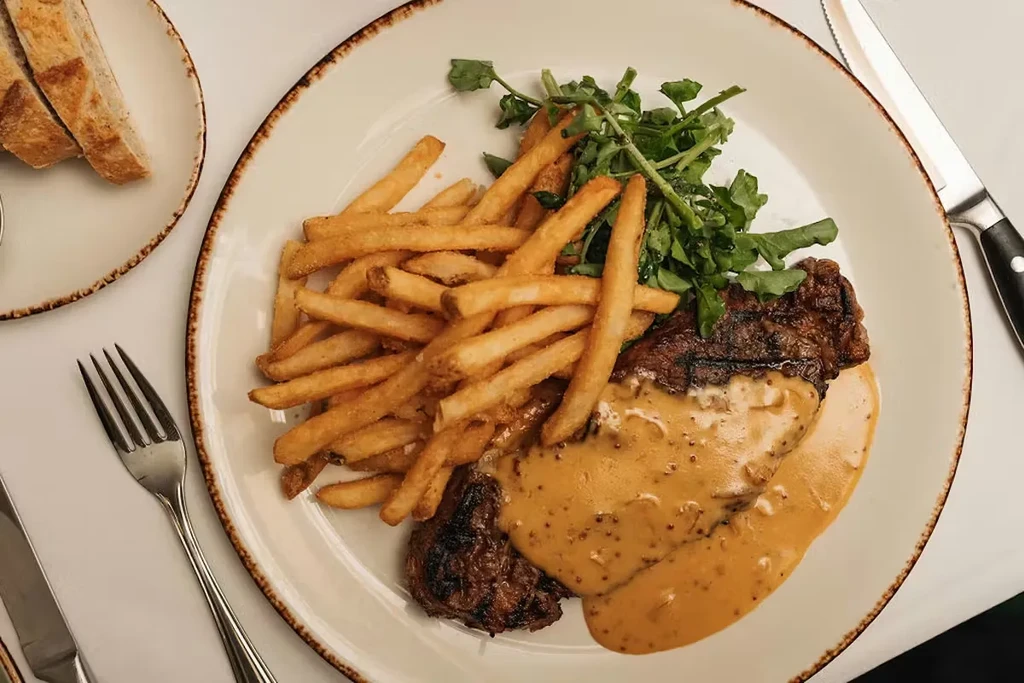 Grilled steak with creamy sauce, golden fries, green salad, and bread.
