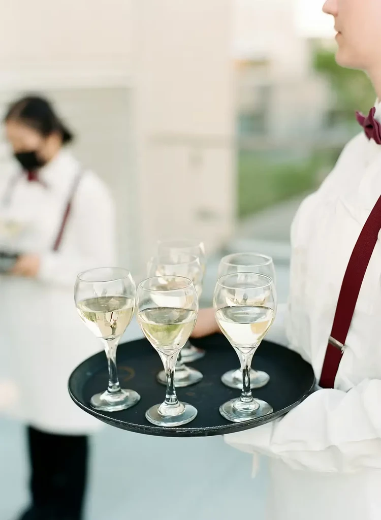 Waiter holds a tray with five glasses of light-colored wine.