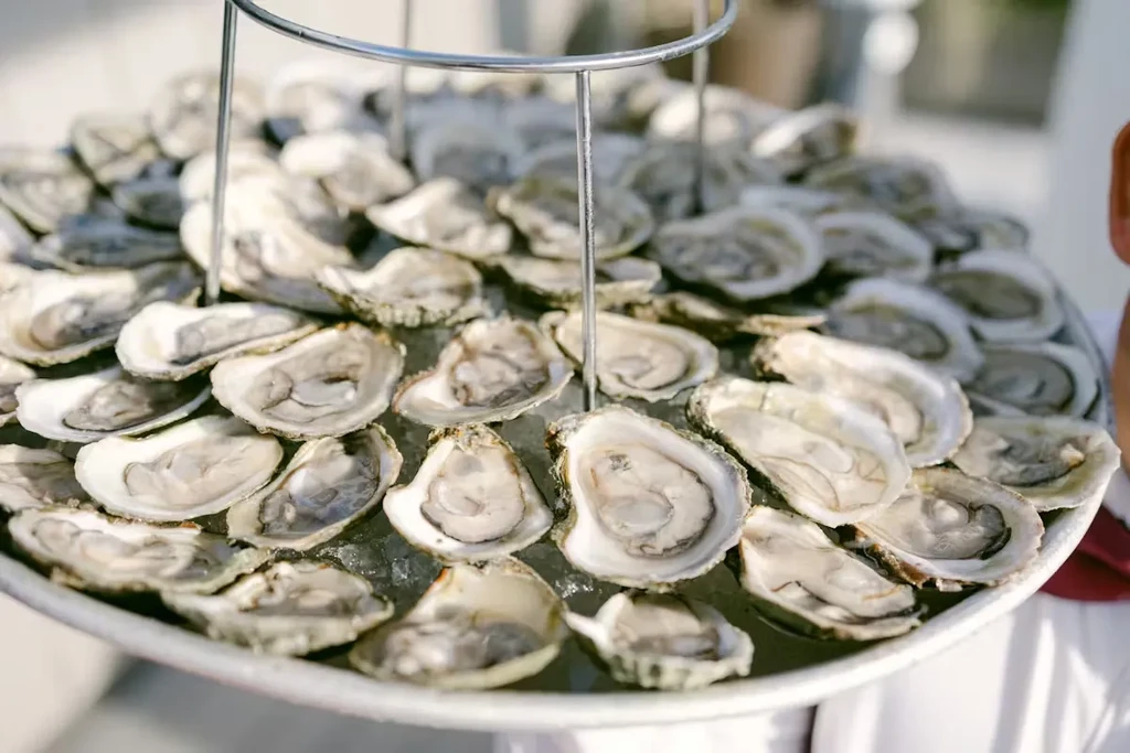 Fresh shucked oysters on a platter of crushed ice with a stand.