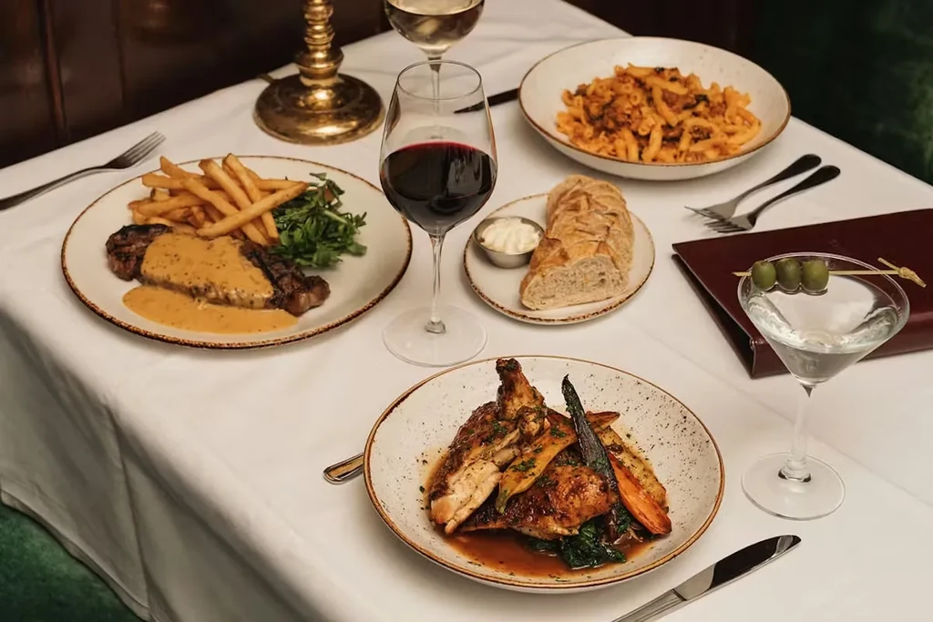 Restaurant table laden with steak, chicken, pasta, wines, and a martini.