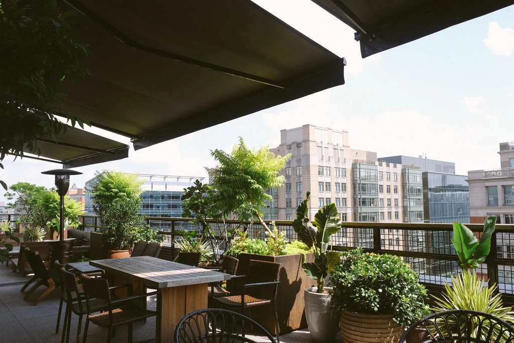 Empty rooftop dining patio with plants, tables, awnings, city skyline.