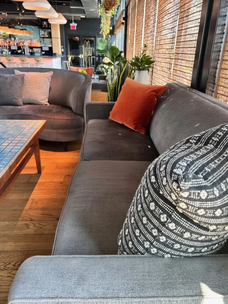 Modern restaurant lounge with sofas, bar area, and sunlit windows.