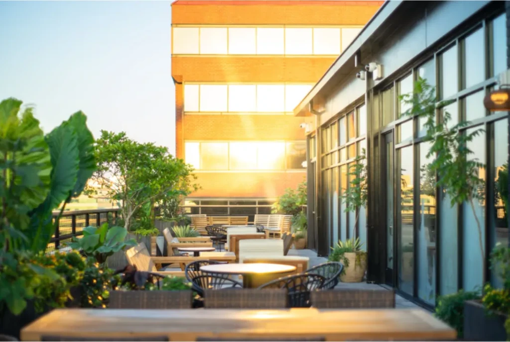 Sunny outdoor patio with dining tables, chairs, potted plants; no people.