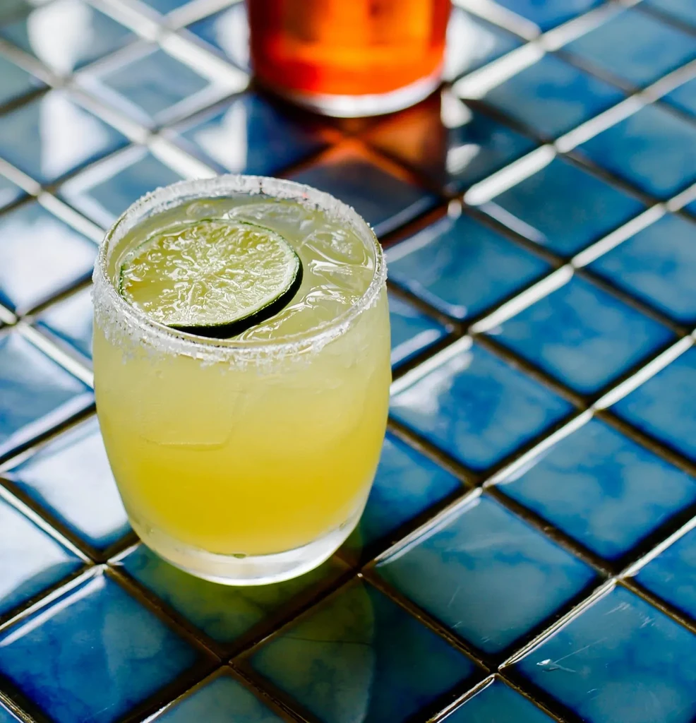 Close-up of margarita with lime and salted rim on blue tiles.