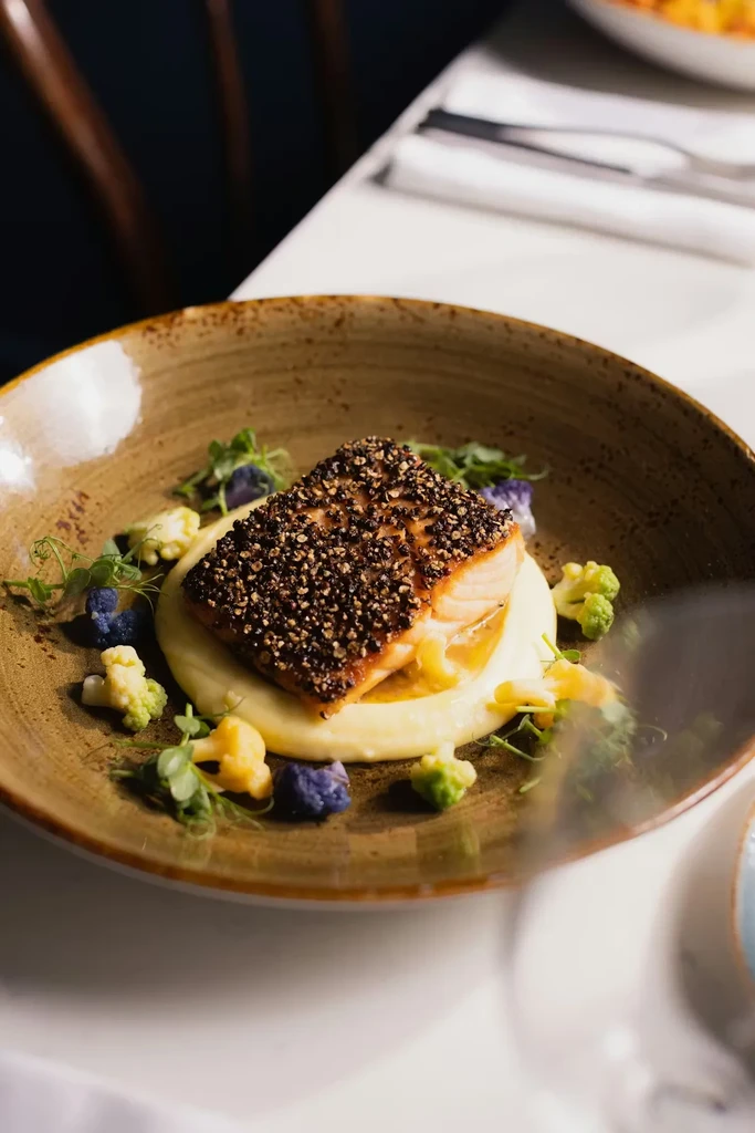 Pepper-crusted salmon, creamy puree, colorful cauliflower, and green microgreens.