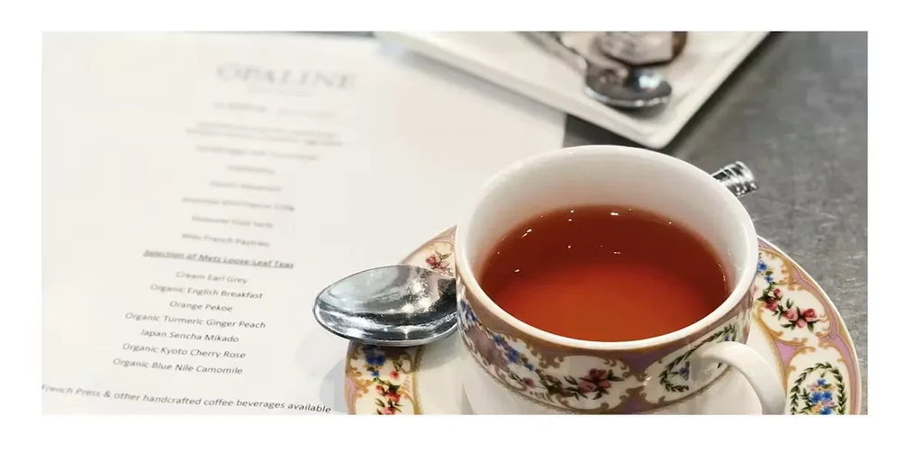 Floral teacup with amber tea, spoon, and blurred menu from 'Opaline'.