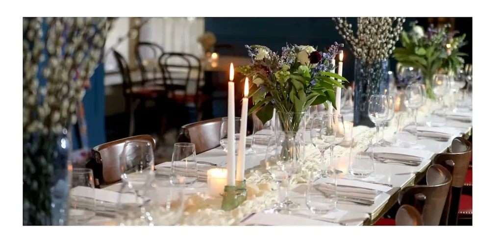 Long dining table elegantly set with lit candles and colorful flowers.