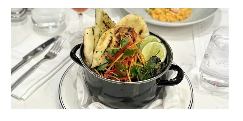 Mussel stew with fresh garnishes and naan in a black pot.