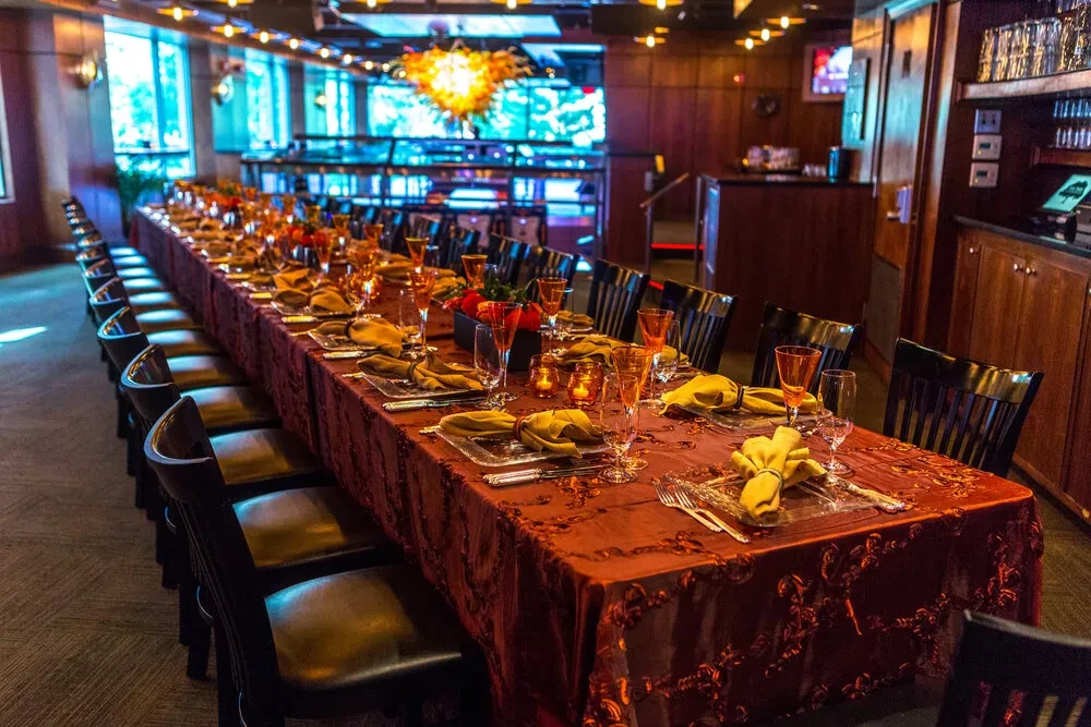 Long, elegantly set table in private room with orange-yellow chandelier.