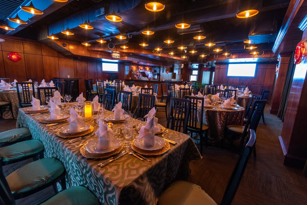 Elegant empty dining room, dark wood, set tables, warm lighting.