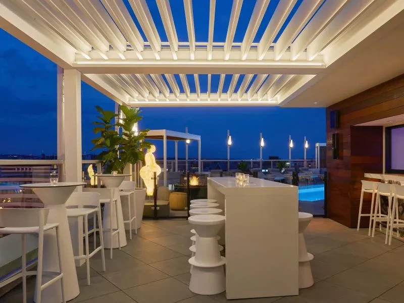 Upscale rooftop bar at twilight with white decor and city skyline.