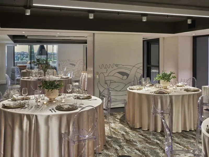 Elegant event space with formally set tables, ghost chairs, city views.