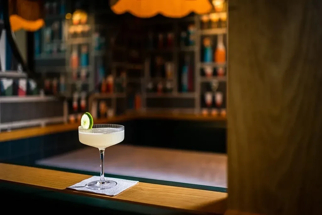Garnished cocktail in ribbed coupe glass on a warmly lit bar.