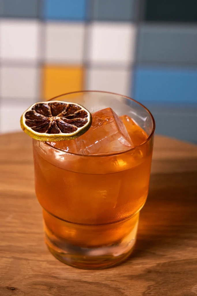 Orange-amber cocktail with ice and dried citrus on wood.