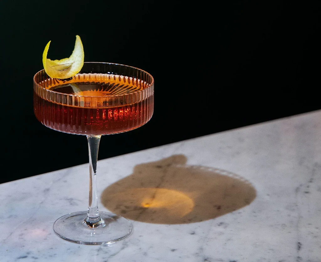 Dark amber cocktail in ribbed coupe with citrus peel on marble.