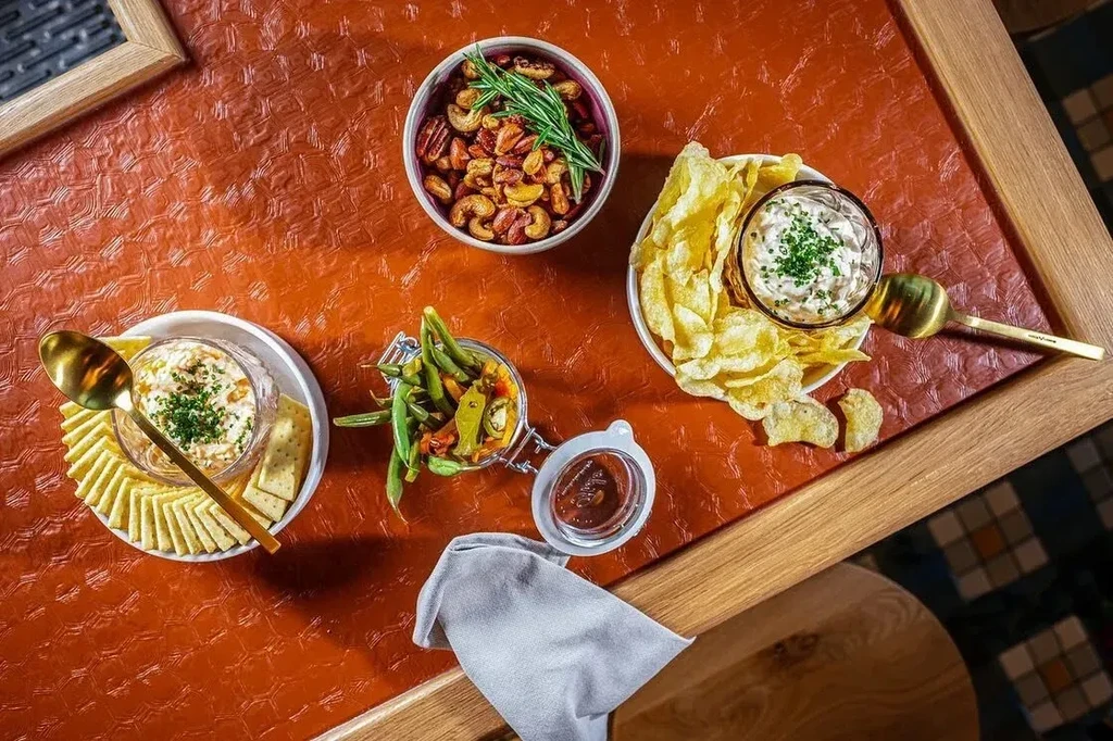 Assortment of appetizers, including nuts, dips, chips, and pickled vegetables.